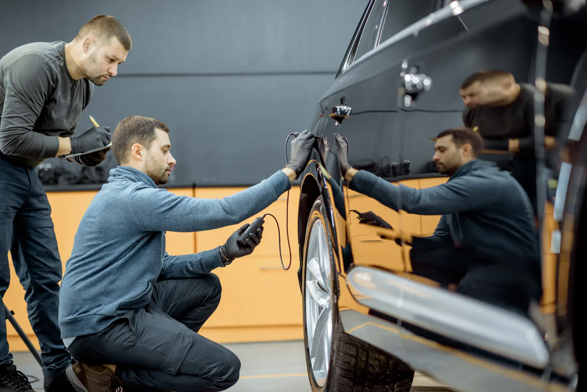 Two car service workers examining vehicle body for scratches and damages while taking a car for professional automotive detailing